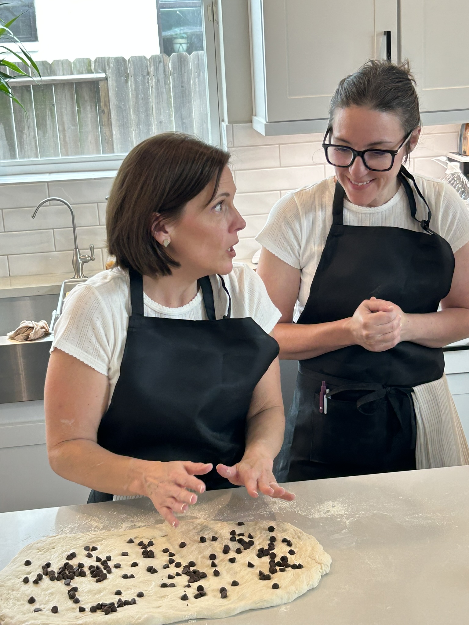 Two guests laughing together while adding chocolate chips to their dough
